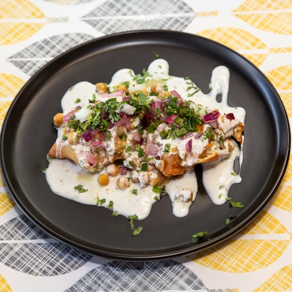 Samosa chaat with yogurt, chickpeas, red onion, and cilantro on a black plate.