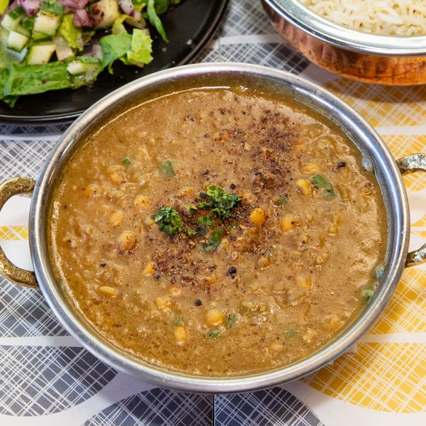 A metal bowl of chana dal, garnished with herbs and spices, alongside a salad and rice.