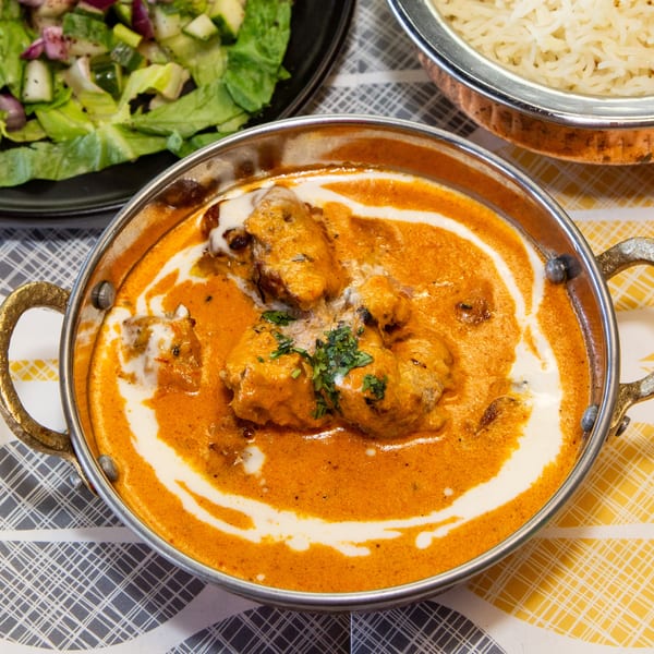 Chicken tikka masala with cream swirls, cilantro, rice, and a side salad on a patterned tablecloth.