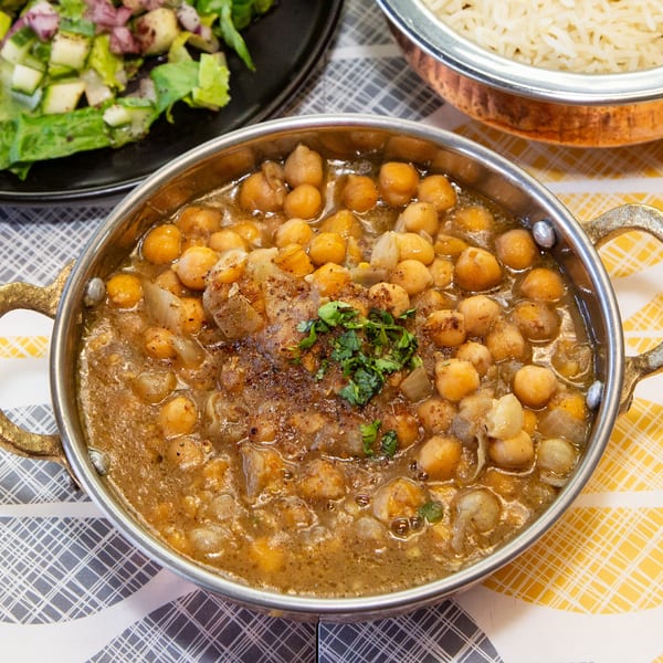 A brass bowl of chickpea curry with cilantro, alongside rice and a green salad.
