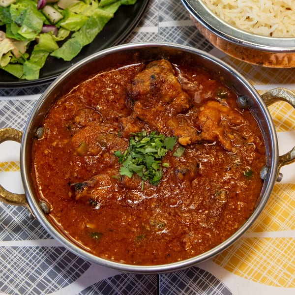 Chicken curry in a metal bowl, garnished with cilantro, served with rice and salad.